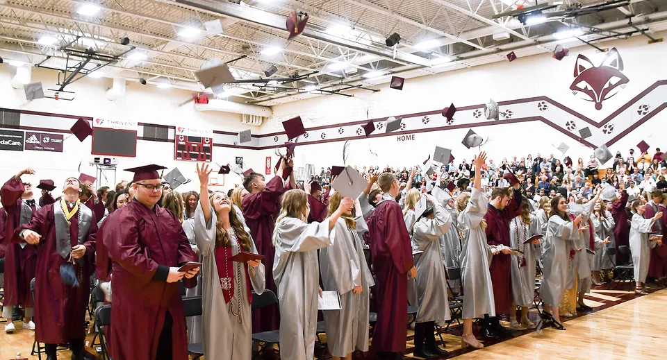 Un grande gruppo di studenti della Fox Valley Lutheran High School è in piedi con le toghe di diploma in una sala decorata.