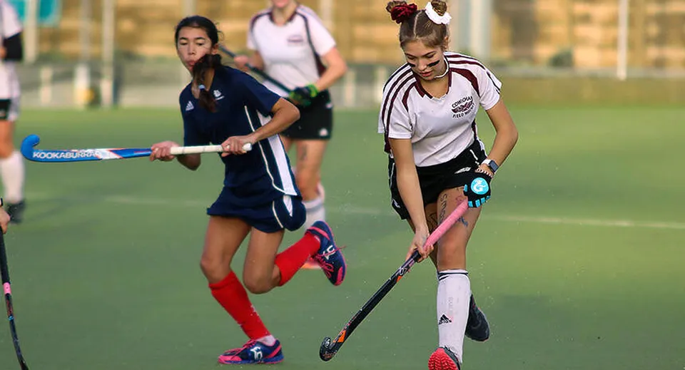 Due studentesse della Lake Cowichan Secondary School giocano una partita di hockey su prato su un campo sportivo.