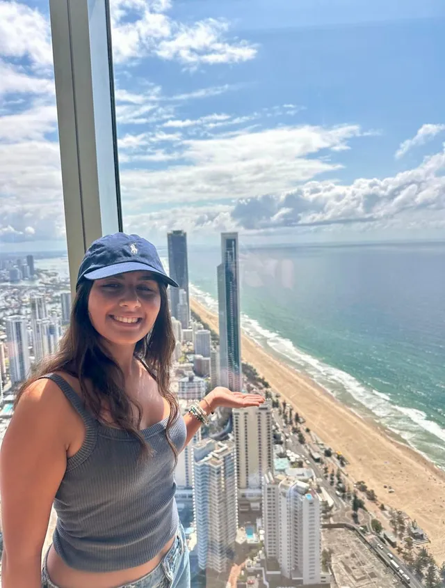 Chica en un mirador acristalado sobre los rascacielos y la larga playa de la costa australiana