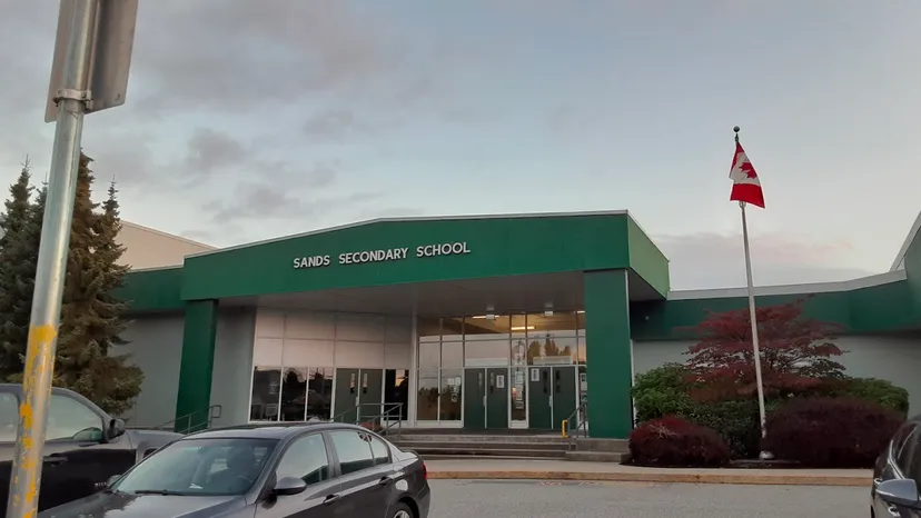 L'edificio scolastico dipinto di verde della Sands Secondary School con una bandiera canadese e alberi nei dintorni.