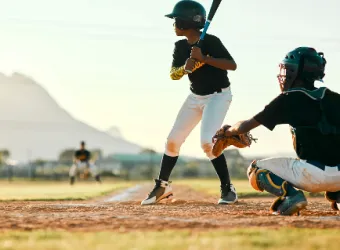 Un bateador de la Ottawa Sports Academy Private School sostiene un bate en el campo de béisbol junto a un receptor.