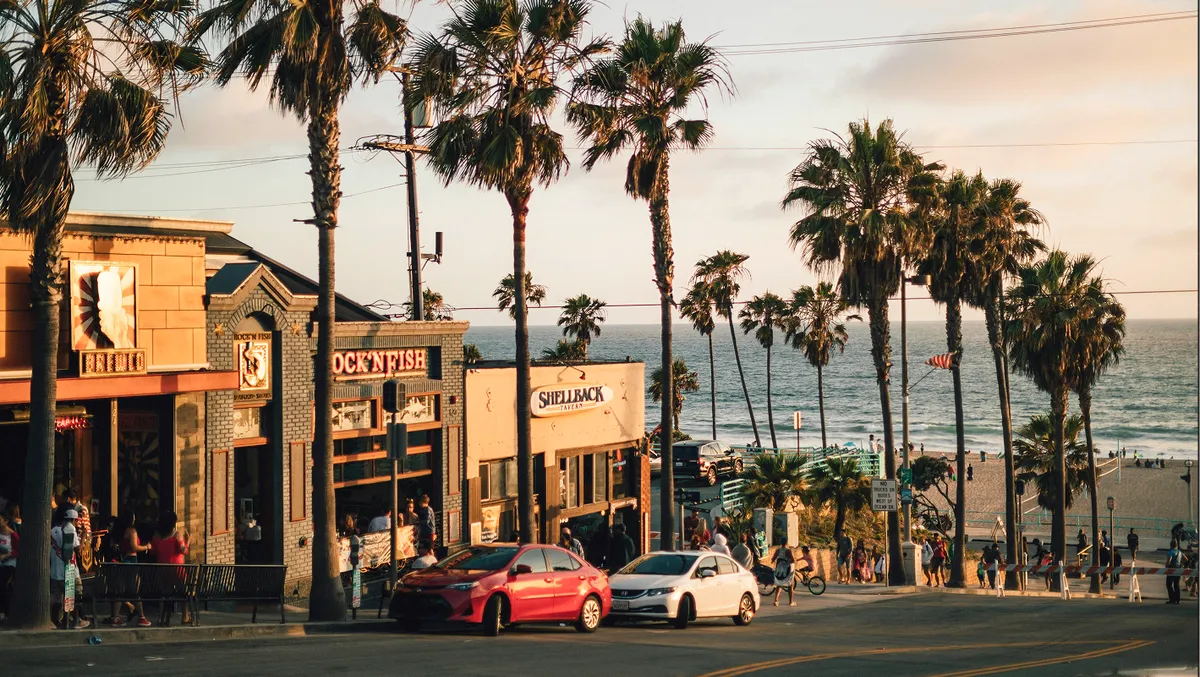 Calle de Los Ángeles al atardecer con palmeras, coches y el paseo marítimo al fondo