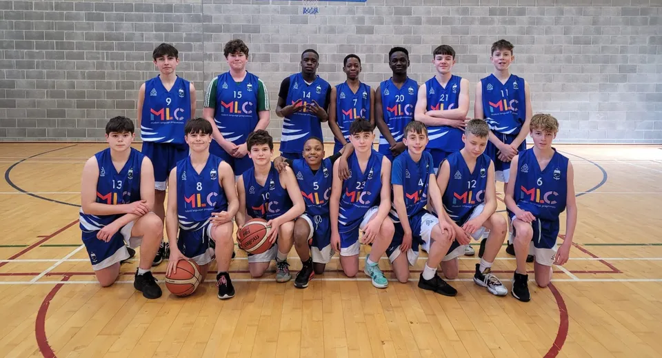 Un gruppo di giovani giocatori e giocatrici di basket posa nella palestra del St. Mel’s College davanti a una parete in mattoni.