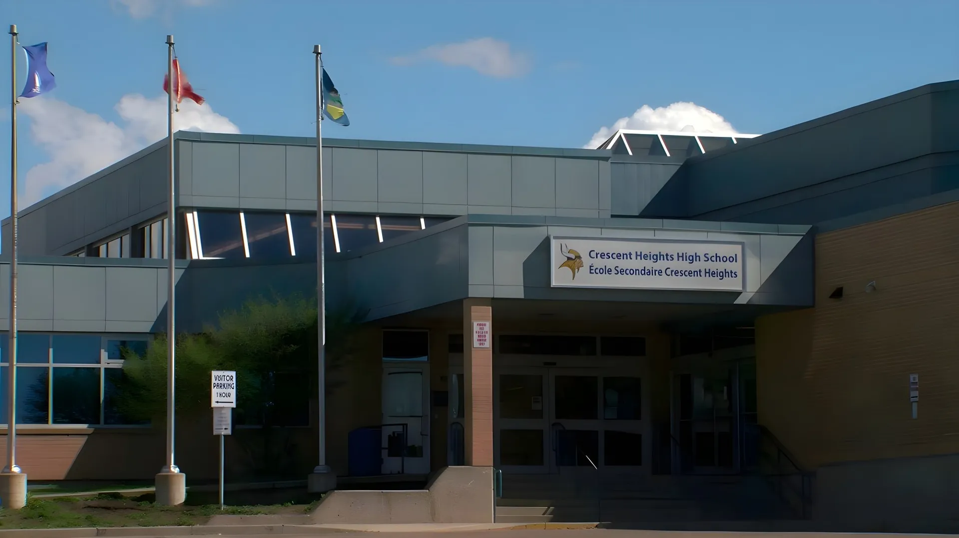 Si vede il moderno edificio scolastico a più piani della Crescent Heights High School con le bandiere che sventolano sul tetto.