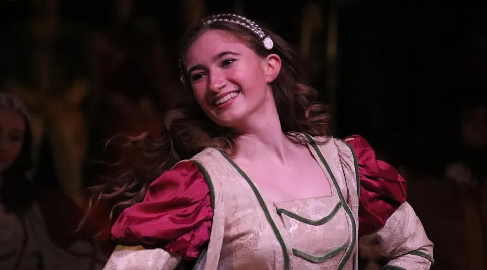 Una studentessa della Emma Willard School con capelli ricci e cerchietti di perle sorride davanti a uno sfondo scuro.