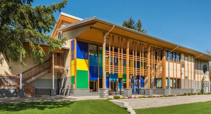 L'edificio moderno e colorato della Queen Margaret’s School sorge su un'area verde con alberi sotto un cielo blu.
