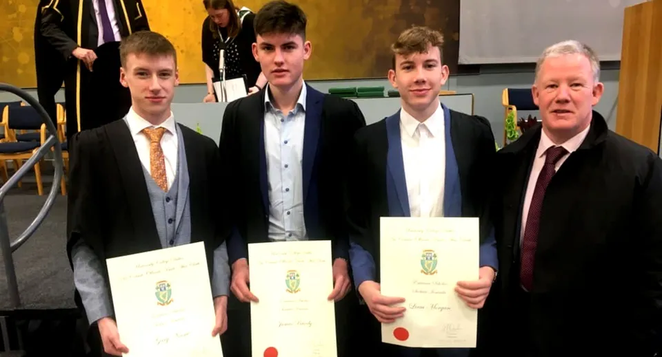 I diplomati del St. Mel’s College in abito formale mostrano i loro diplomi durante la cerimonia di diploma insieme a un ospite d'onore.