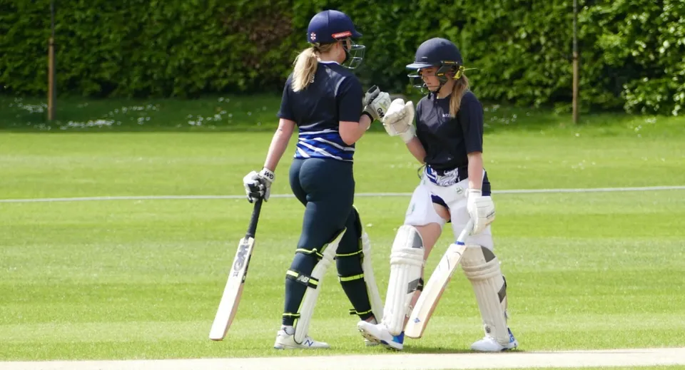 Due giocatrici di cricket del Wrekin College con attrezzatura protettiva e mazze su un campo in erba.