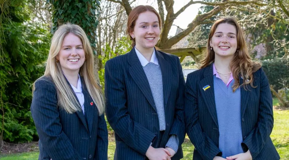 Tre studentesse in divisa scolastica del Kent College Pembury sono insieme e sorridono nel bosco.