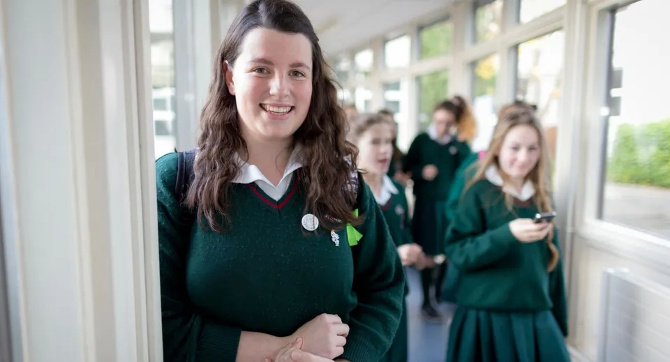 Una studentessa del St. Leo’s College in divisa verde sorride in un corridoio della scuola.