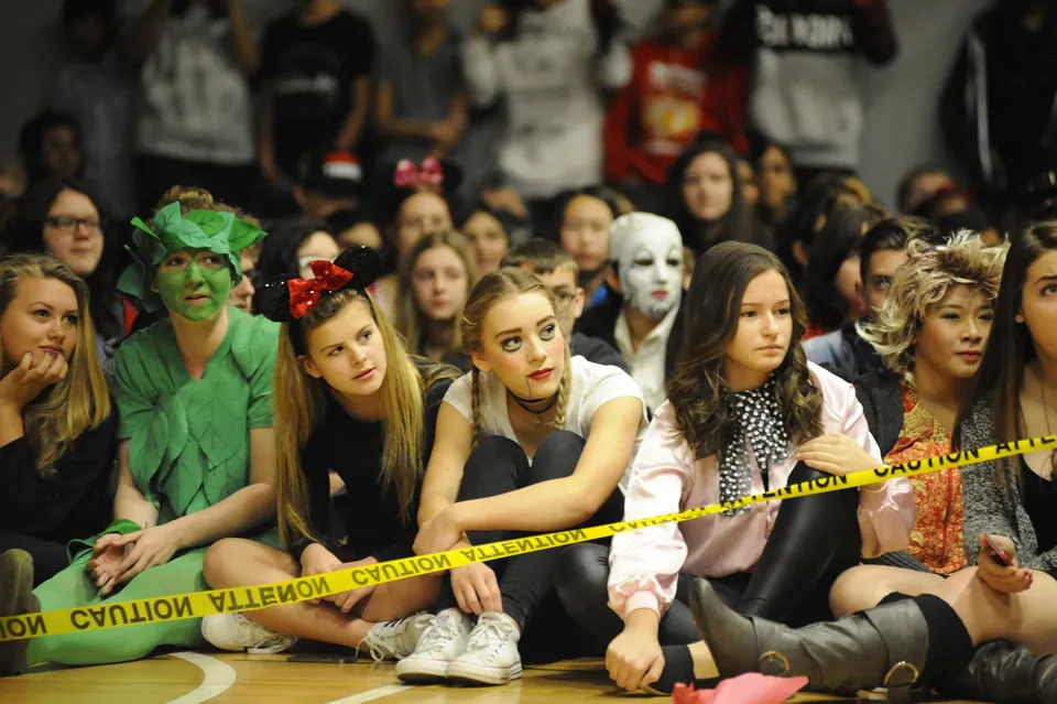 Un gruppo di persone in costume siede dietro una transenna della polizia durante un evento alla W.J. Mouat Secondary School.