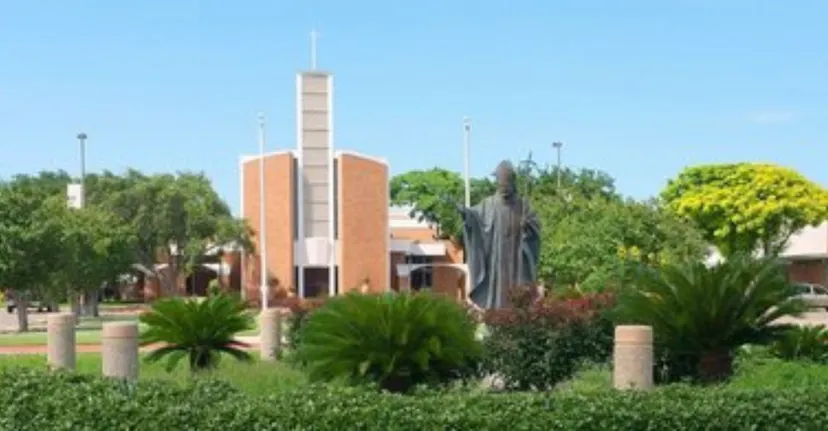 L'edificio moderno della St. John Paul II High School si erge con un'alta torre immerso nel verde tra palme e altra vegetazione.