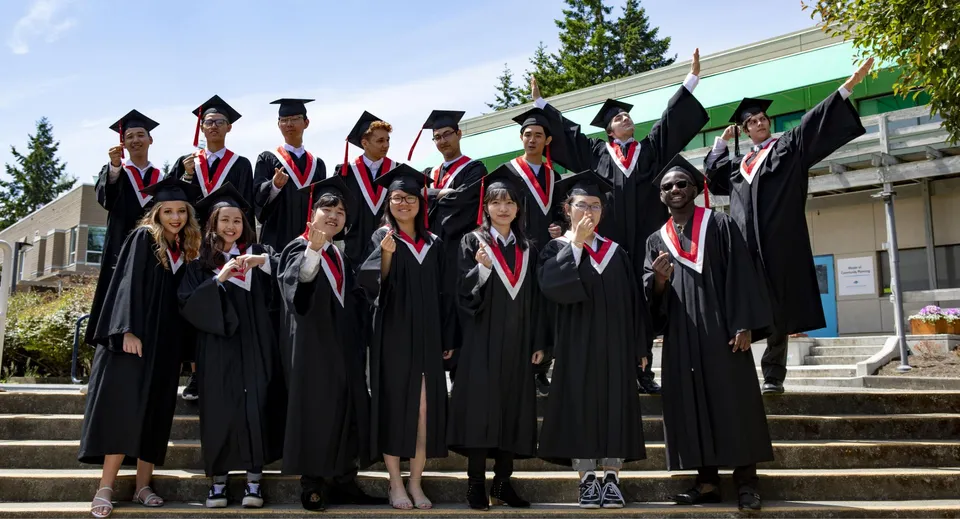 I diplomati della Centre Dufferin District High School sono in piedi sulle scale dell'edificio scolastico indossando toghe nere con stole rosse.