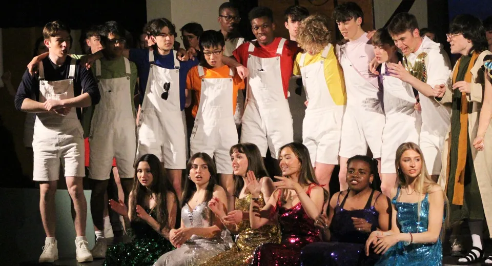 Un gruppo di studentesse e studenti è in piedi sul palco del Wesley College, presentandosi con abiti colorati.