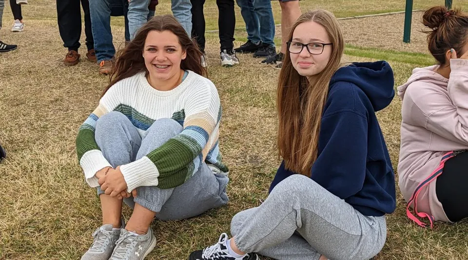 Due studentesse della Tofield School siedono sorridenti sull'erba all'aperto.