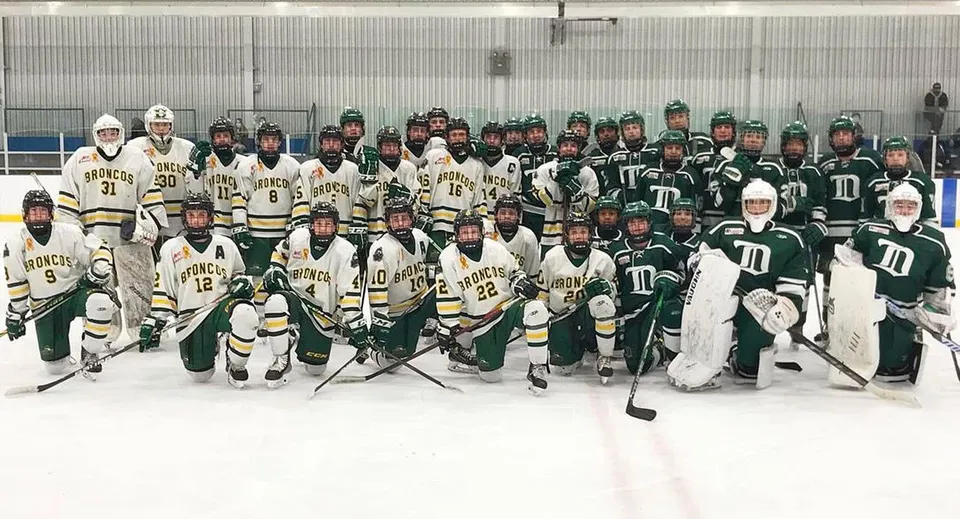 La squadra di hockey della North Delta Secondary School posa insieme sulla pista da ghiaccio davanti a una parete metallica.