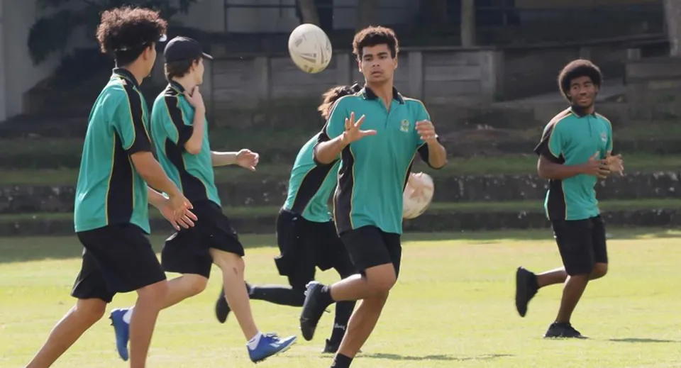 Studenti della Sunnybank State High School giocano a rugby su un campo sportivo con l'edificio scolastico sullo sfondo.