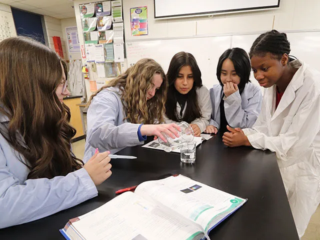 Estudiantes de la Brocklehurst Secondary School examinan juntas algo en una mesa de laboratorio en el aula.