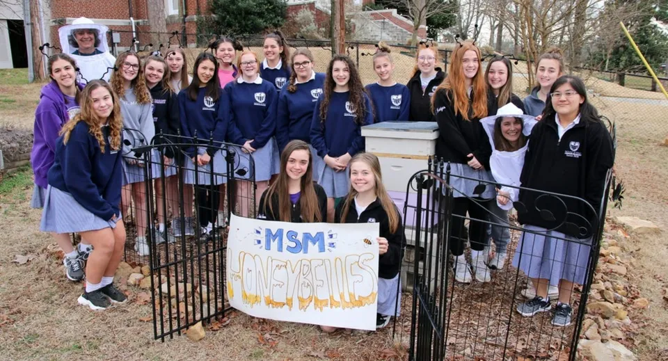 Un gruppo di studentesse della St. Mary Catholic High School si trova con uno striscione davanti a un edificio in mattoni.