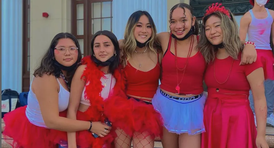 Un gruppo di giovani donne con outfit rossi posa davanti a un edificio del campus dell'Alameda Unified School District.