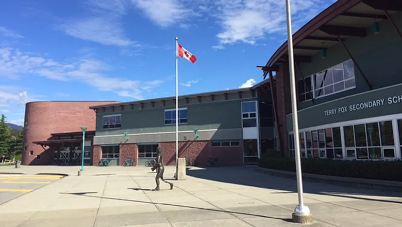 L'edificio scolastico a più piani della Terry Fox Secondary School con la bandiera canadese e persone in primo piano.