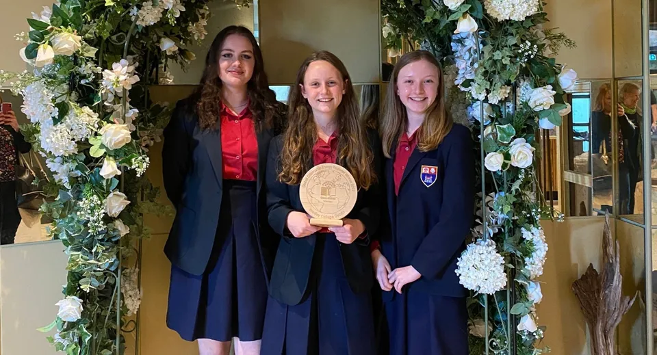 Tre diplomate del Wesley College sono in piedi insieme davanti a un arco decorato con fiori, tenendo in mano il loro diploma.