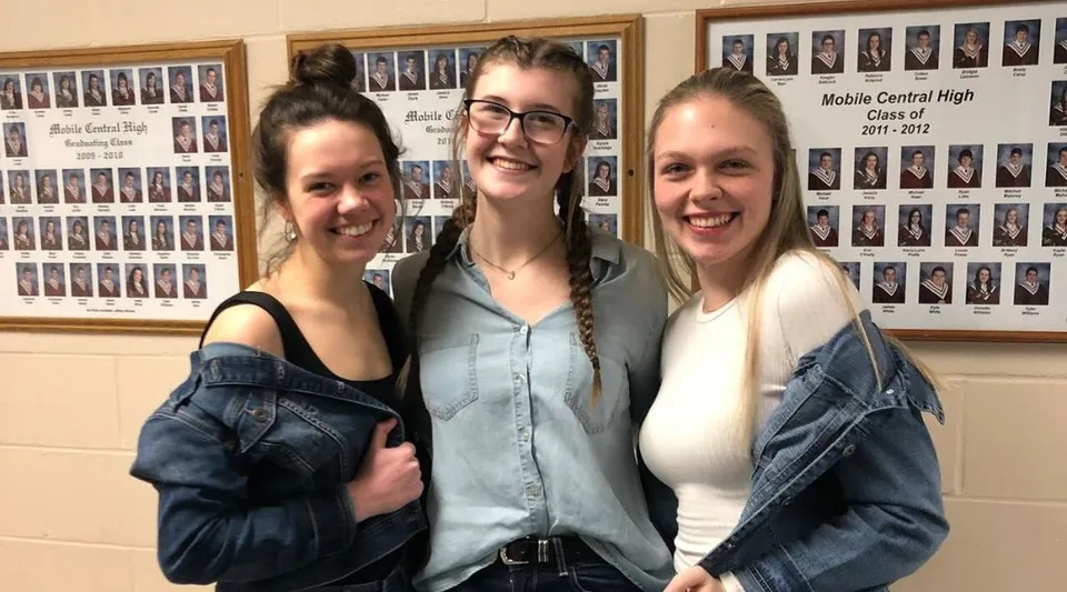 Tre studentesse sono insieme davanti a una parete con le foto di classe alla Mobile Central High.