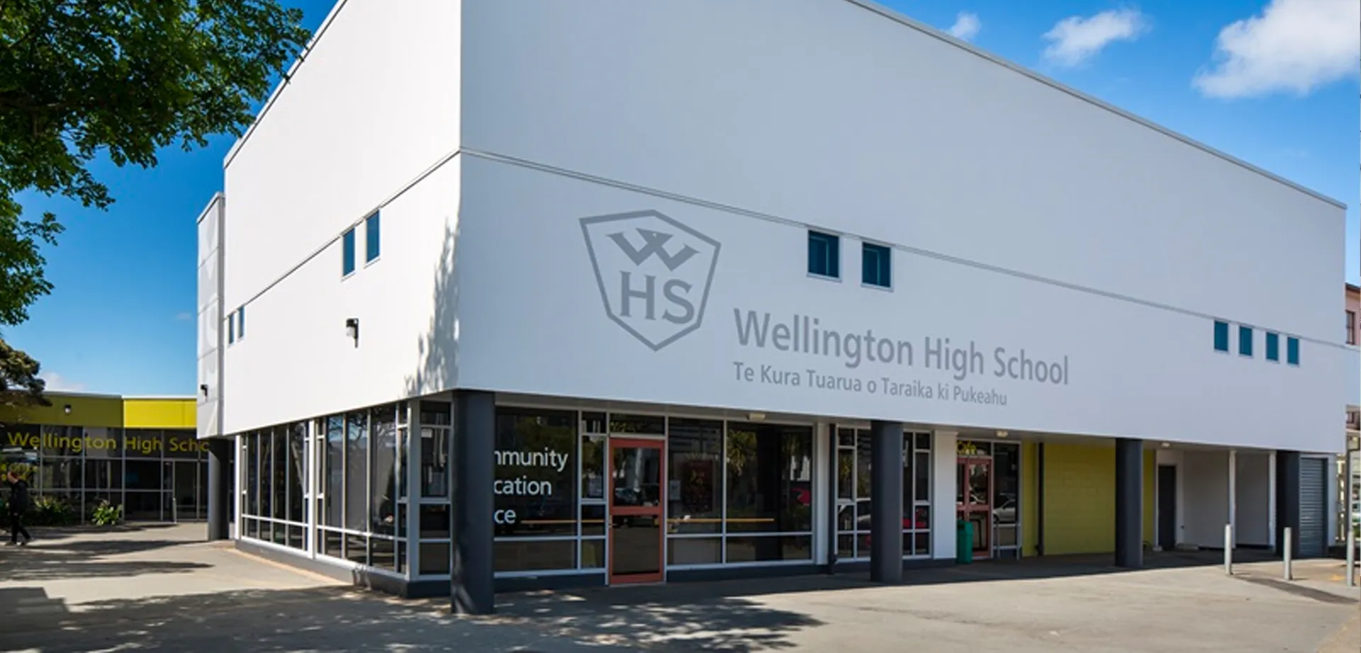 L'edificio bianco e moderno della Wellington High School si erge sotto un cielo blu circondato da alberi.