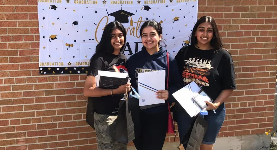 Tre studentesse del West Humber Collegiate Institute sono in posa davanti a uno sfondo per la cerimonia di diploma, tenendo con orgoglio i loro diplomi.