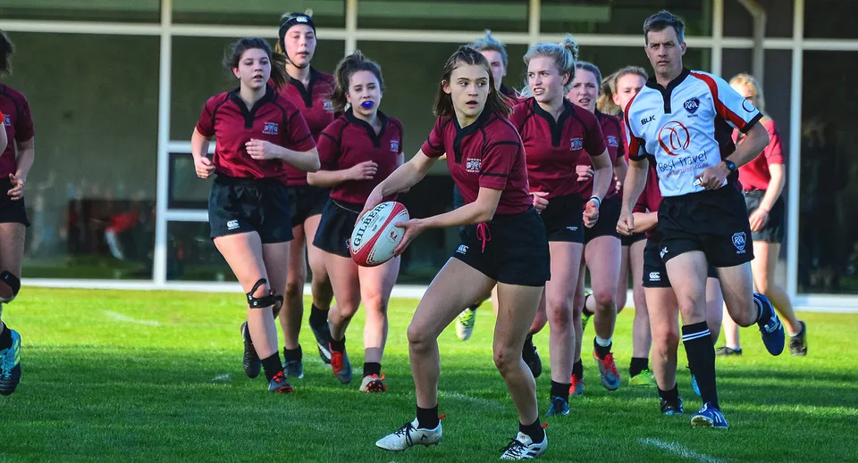 Un gruppo di giocatrici di rugby della Chemainus Secondary School si trova su un campo in erba con una squadra avversaria sullo sfondo.