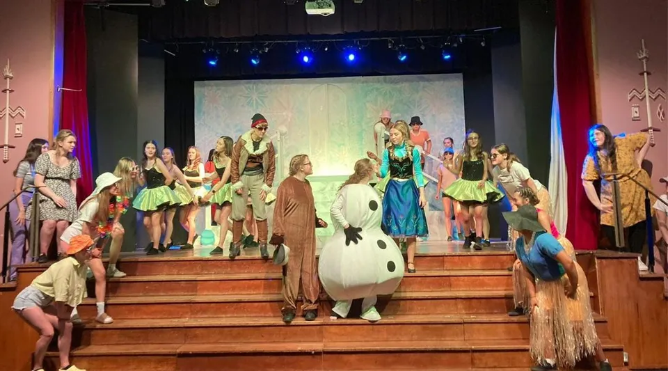 Un gruppo di studenti della St. Louis Secondary School sta in costumi colorati sul palco davanti a una scenografia dipinta.