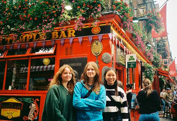 Tres chicas sonrientes ante el pub Temple Bar decorado con flores en Dublín