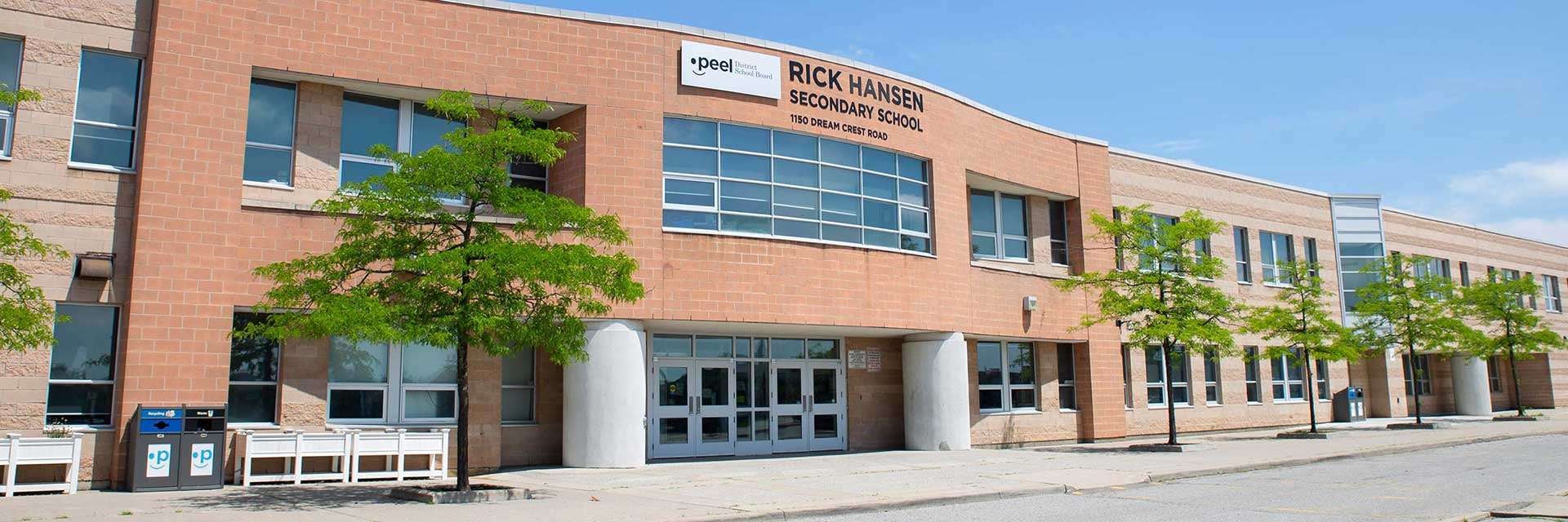 Backsteingebäude der Rick Hansen Secondary School mit Bäumen die vor der Schule entlangwachsen.