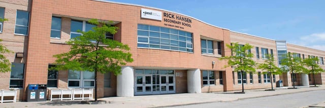 Backsteingebäude der Rick Hansen Secondary School mit Bäumen die vor der Schule entlangwachsen.