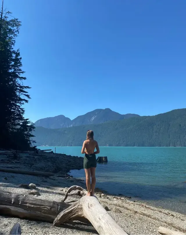 Studentessa su un tronco osserva un lago turchese tra le montagne durante un anno all'estero in Canada