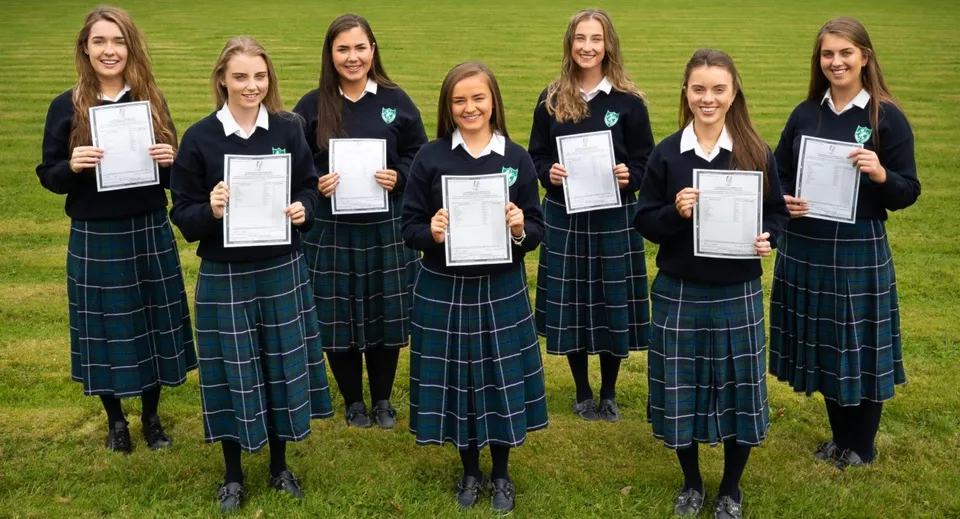 Un gruppo di studentesse della Salerno Secondary School si trova su un campo erboso tenendo in mano dei certificati.