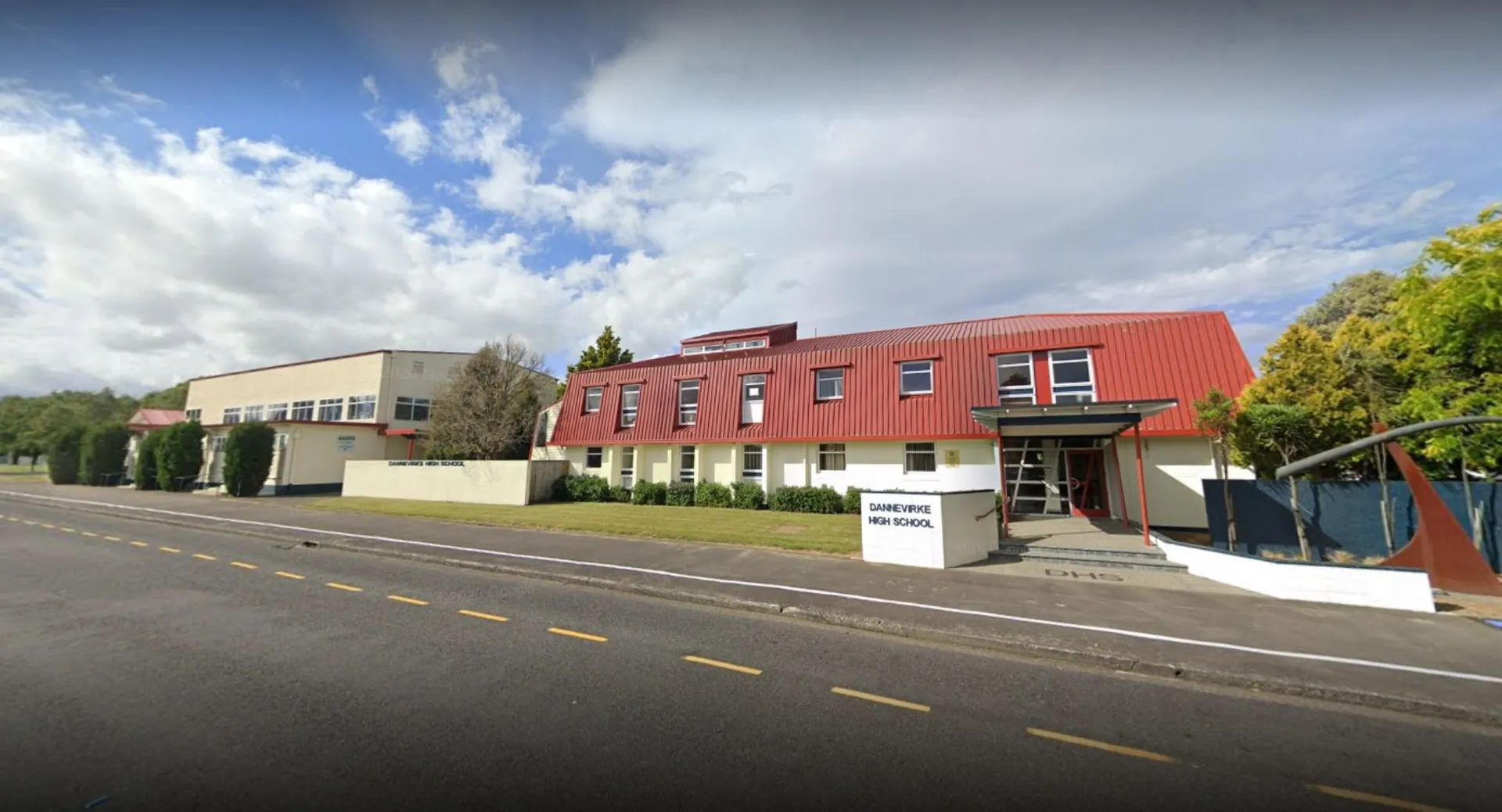 L'edificio moderno a più piani della Dannevirke High School con facciata rossa si trova lungo una strada ed è circondato da alberi.