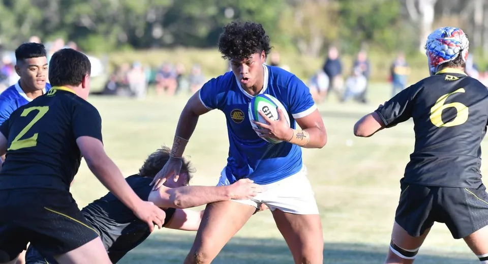 Un gruppo di studenti gioca a rugby sul campo del St. Edmund’s College con alberi ed edifici sullo sfondo.