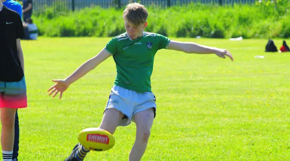 Un alunno della St Ailbe's School corre su un campo erboso giocando con un pallone da calcio.