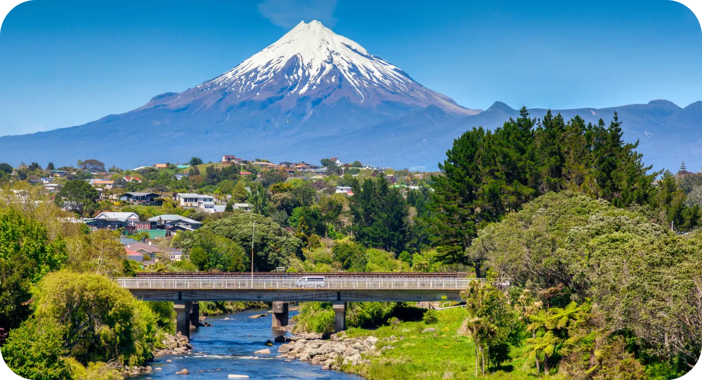 Volcán nevado de forma cónica sobre una pequeña ciudad con un río y un puente en primer plano