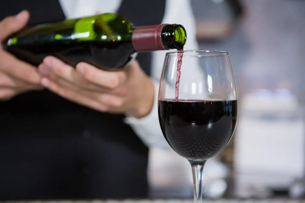 Kellner schenkt Rotwein aus einer Flasche in ein Weinglas ein