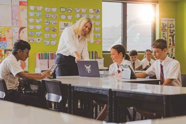 Una profesora muestra algo en un portátil a estudiantes con uniforme de la Lindisfarne Anglican Grammar School en un aula.