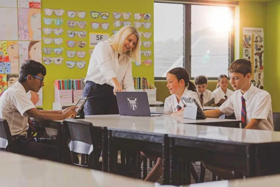 Un'insegnante mostra qualcosa su un laptop agli studenti in uniforme della Lindisfarne Anglican Grammar School in un'aula.