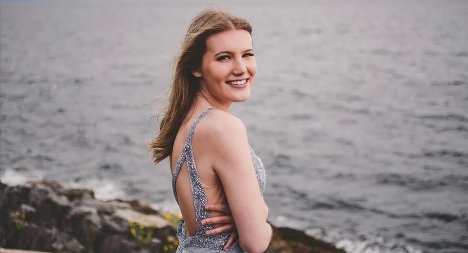 Una giovane donna sorride davanti a un paesaggio roccioso con cielo nuvoloso nel campus della Kwalikum Secondary School.