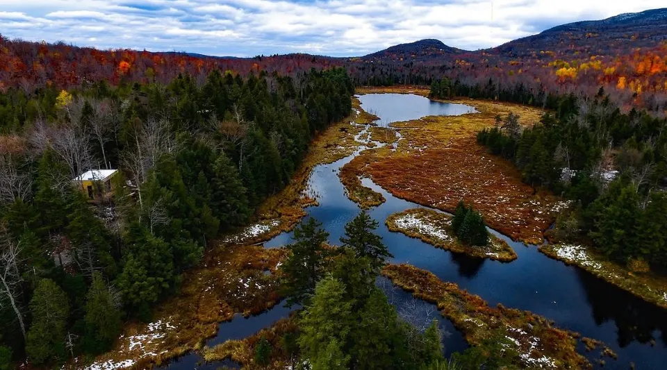 Un paesaggio fluviale autunnale con alberi colorati e montagne sullo sfondo nel terreno della Polyvalente W.-A.-Losier.
