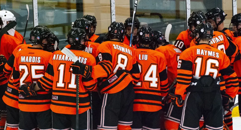 Un gruppo di giocatori di hockey in maglie arancioni si trova insieme davanti a un edificio nel campus del Ridley College.