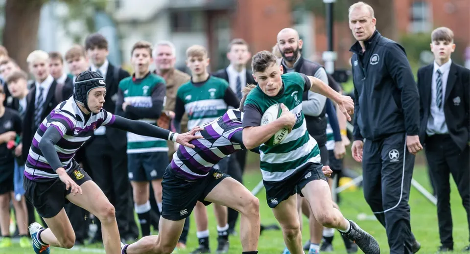 Gli studenti della Luckley House School giocano una partita di rugby con spettatori e allenatori sullo sfondo.