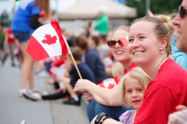 Una mujer sonriente y una niña sentadas en la calle sosteniendo una pequeña bandera canadiense