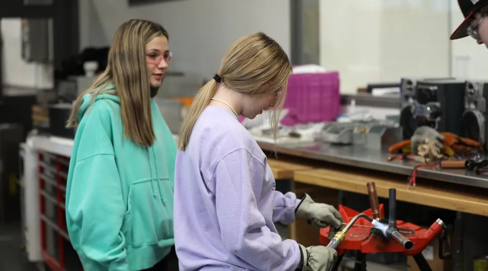 Due studentesse del Boise School District si trovano in un laboratorio con vari oggetti e attrezzature sullo sfondo.