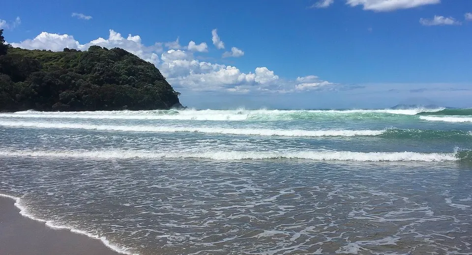 Un paesaggio di spiaggia con onde, rocce e cielo blu vicino al Waihi College.